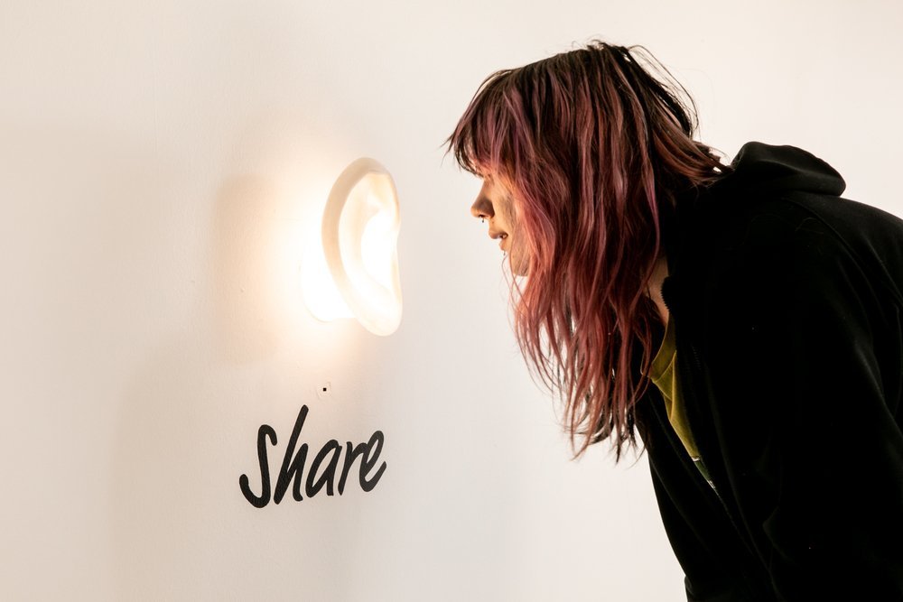 Participant whispering a fear into a sculptural ear labelled 'Share', Fear Exchange